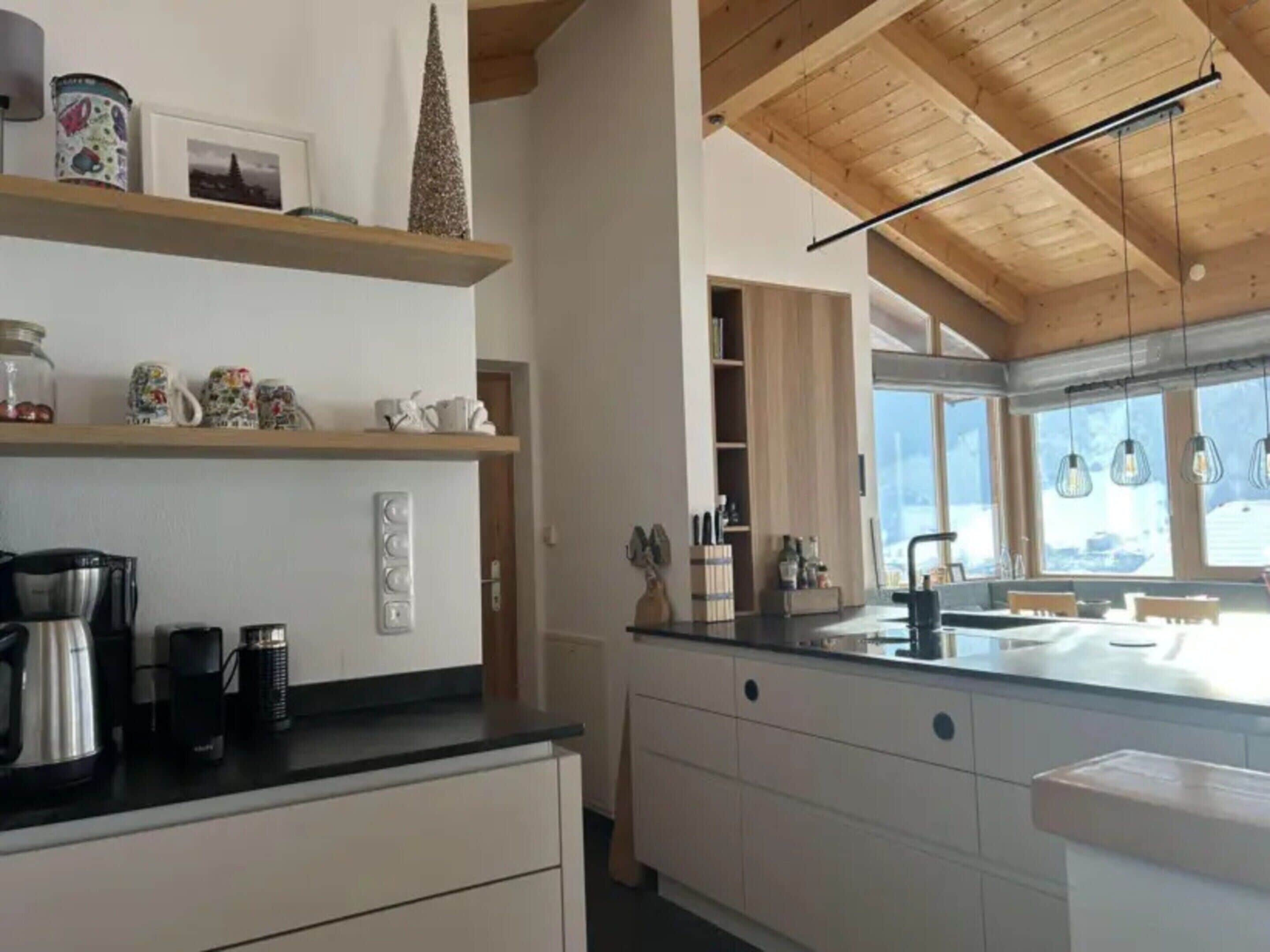 A modern kitchen with wooden beams, a black countertop, and a large window.