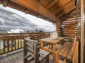 Terraza de madera con bancos y una mesa, con vista a un paisaje nevado y edificios al fondo.