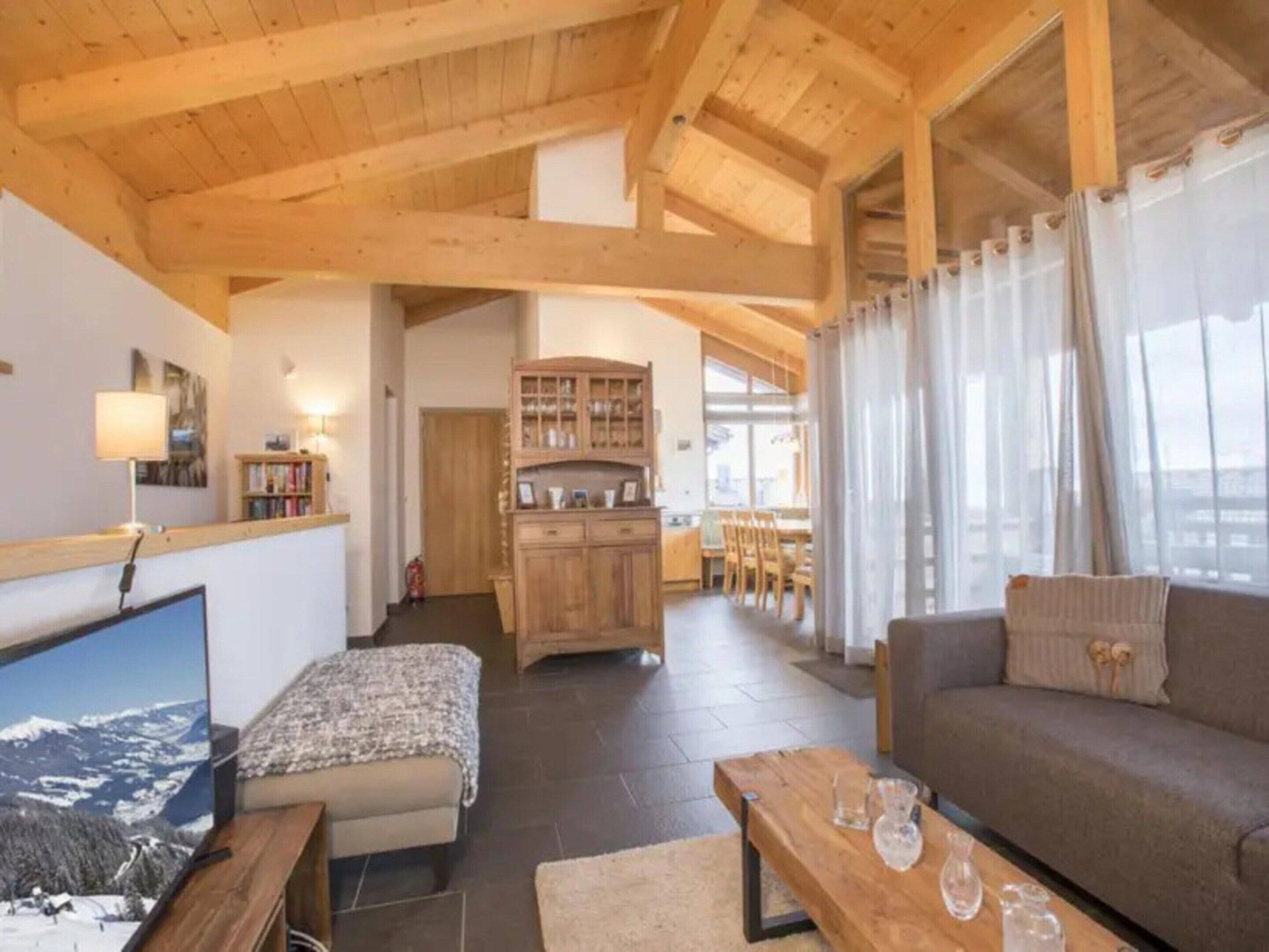 Uma sala de estar aconchegante com uma televisão de tela plana grande, um sofá, uma mesa de centro de madeira e uma estante de livros.