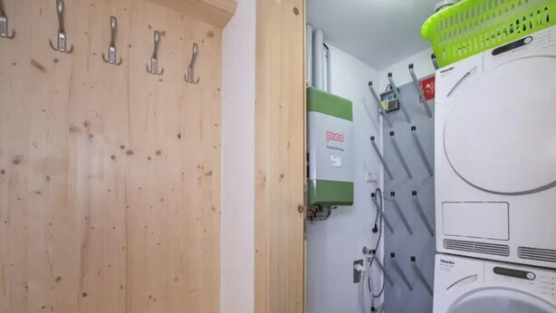 Une buanderie équipée d’un lave-linge, d’un étendoir et d’une armoire en bois avec des crochets.