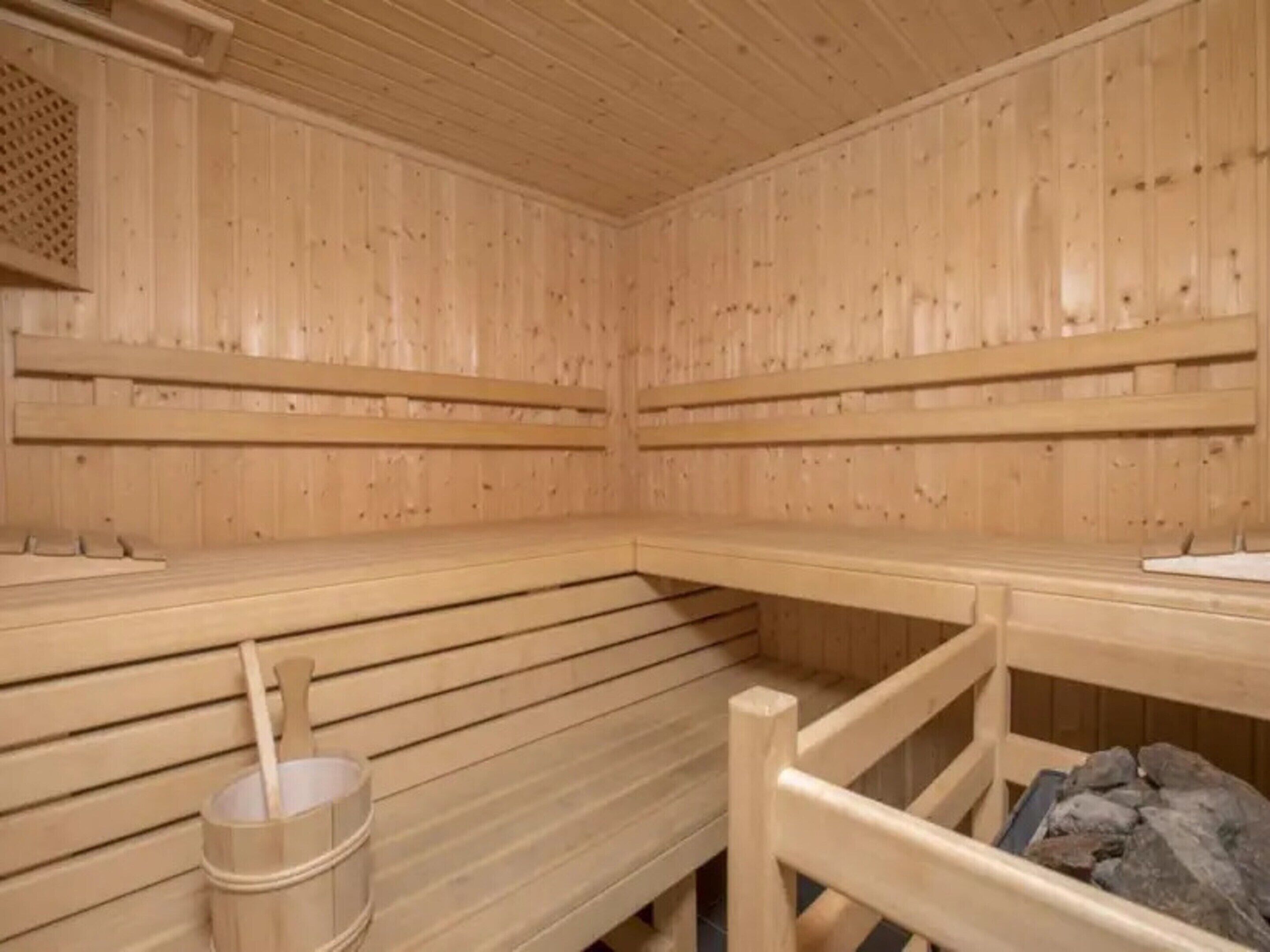 A sauna room with wooden walls, benches, a bucket, and a pile of rocks.