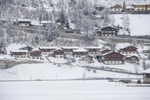 Un pueblo cubierto de nieve con edificios de estilo chalete tradicional, un telesilla y un paisaje de montañas al fondo.