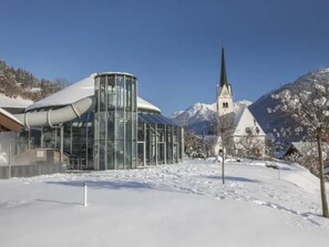 A modern building with a glass facade and a church with a steeple in the background. - Austrian Mountain Chalet Retreat (Wald im Pinzgau)