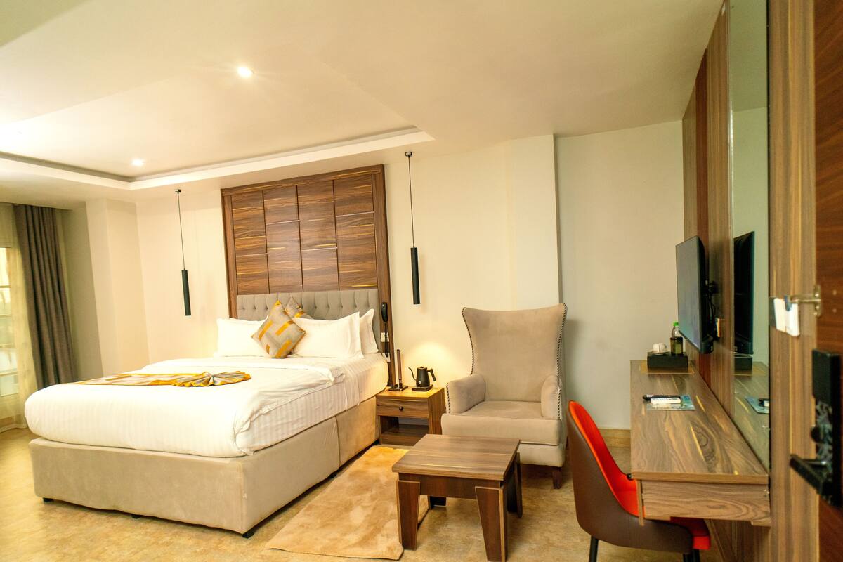A hotel room with a large bed, a desk with a chair, a TV, and a wooden headboard.