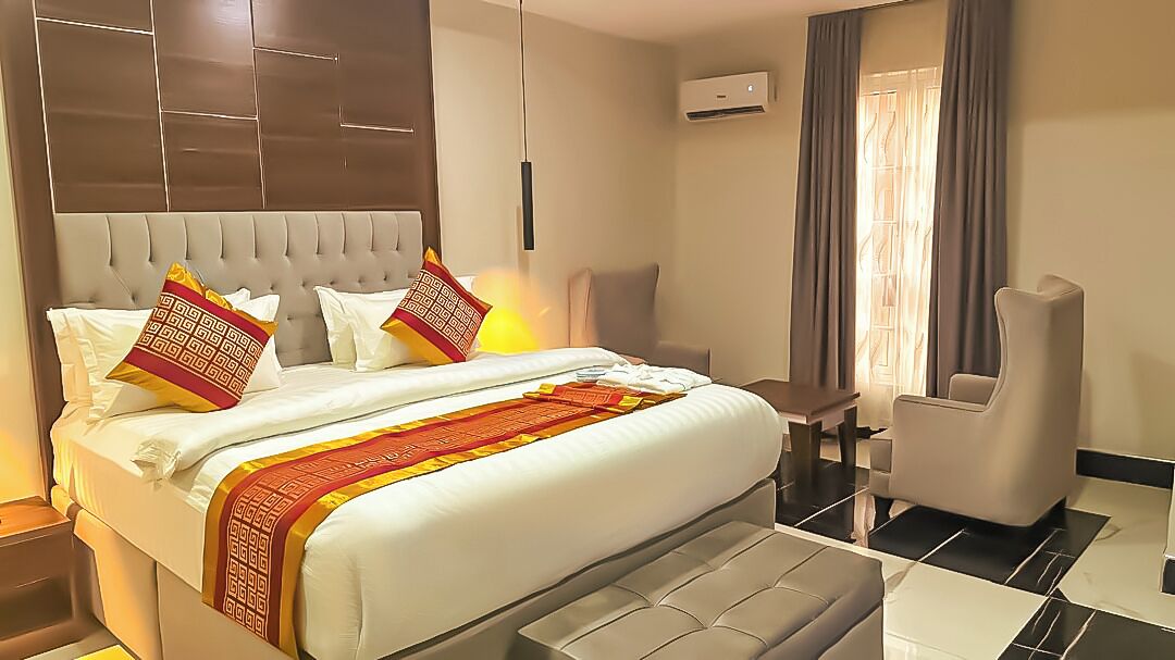 A hotel room with a large bed, a chair, a desk, and a window with curtains.