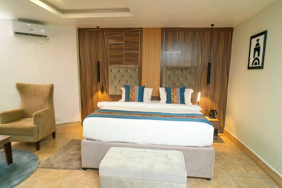 A bedroom with a large bed, a chair, a bedside table, and a wall-mounted air conditioner.