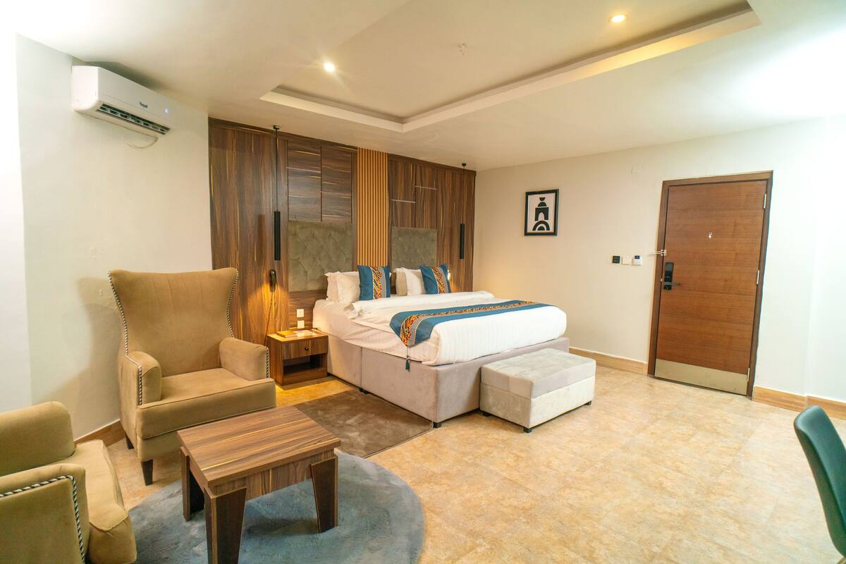 A hotel room with a bed, a sofa, a small table, and a wooden door.