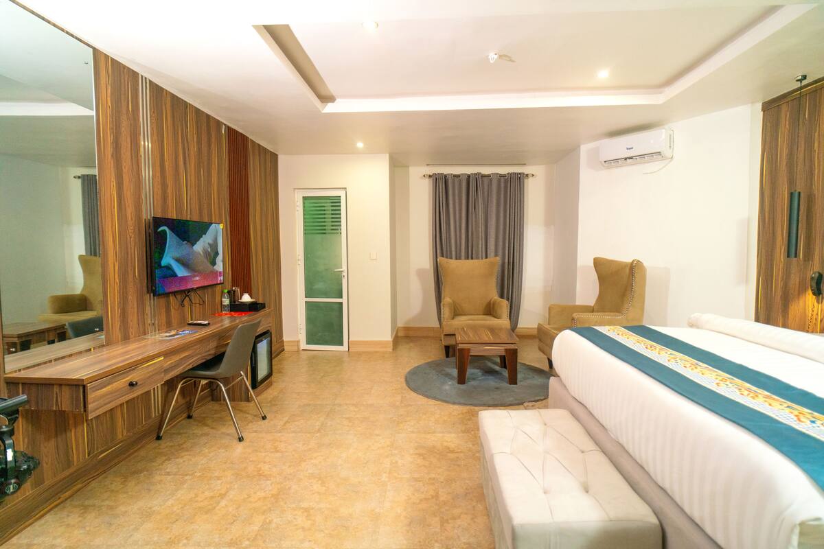 A hotel room with a wooden desk, a television, a sofa, a bed, and a bathroom door.
