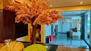 A lobby with a large artificial cherry blossom tree, a reception desk, and a glass partition. - Tribu Hotel (Enugu)