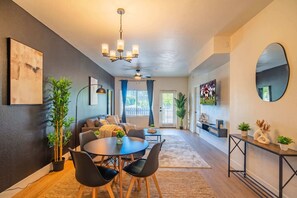 A modern living room with a dining area, a ceiling fan, and a large mirror on the wall.