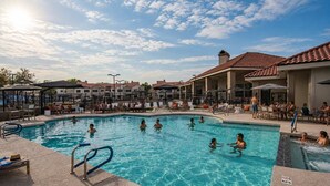 A swimming pool with people, lounge chairs, and umbrellas.