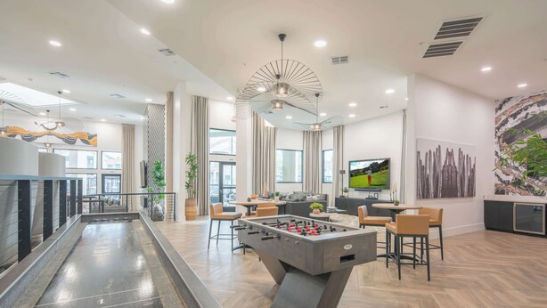 A modern indoor space with a foosball table, a pool table, and a bar area.