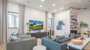 A modern living room with a large flat-screen TV, grey sofas, a coffee table, and a dining area with a table and chairs. - Stay Near TPC Pool,Balcony,Pickleball,Parking,WD (Scottsdale)