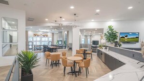 A modern hotel lobby with round tables, comfortable seating, a kitchen area, and a TV mounted on the wall. - Stay Near TPC Pool,Balcony,Pickleball,Parking,WD (Scottsdale)