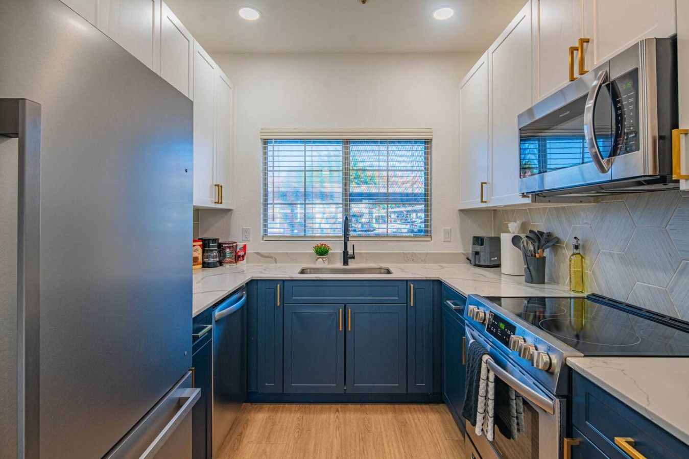 Una cocina moderna con una isla central, electrodomésticos de acero inoxidable y un ventanal con persianas.