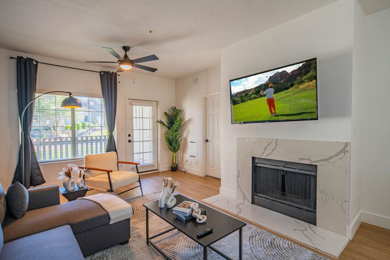 A living room with a sofa, armchair, coffee table, television, fireplace, and a ceiling fan.