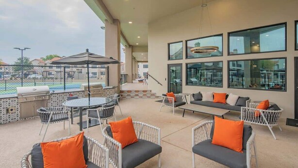 Ein Außenbereich mit einer Terrasse, Korbmöbeln, einem Grill und einem Pool im Hintergrund.