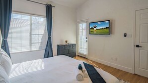 Ein Schlafzimmer mit Bett, Vorhängen, Deckenventilator, Fernseher, Kommode und einer Tür.