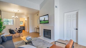Ein modernes Wohnzimmer mit Kamin, Essbereich und einer Küche im Hintergrund.