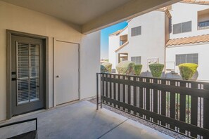 Un balcon avec une balustrade noire, une porte avec une fenêtre, et un bâtiment avec de nombreuses fenêtres et un toit recouvert de tuiles en arrière-plan.