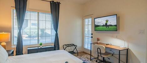 A hotel room with a bed, a desk, a television, and a window with curtains.