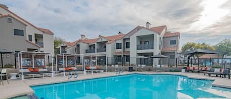 A swimming pool with lounge chairs and umbrellas, surrounded by multi-story buildings with balconies.