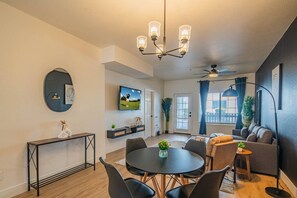 A modern living room with a dining area, a TV mounted on the wall, and a ceiling fan.