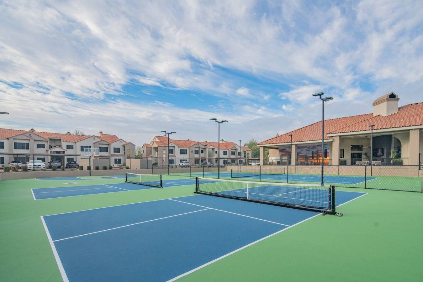 A tennis court with a net, surrounded by buildings with red-tiled roofs.