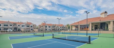 A tennis court with a net, surrounded by buildings with red-tiled roofs.