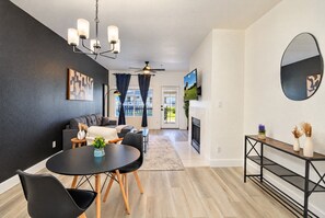 Un salon moderne avec un mur de couleur sombre, une cheminée, un coin repas avec une table ronde et des chaises, et un grand miroir accroché au mur.