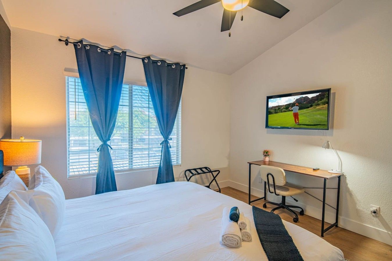 Une chambre d’hôtel avec un lit, un bureau, une chaise, une télévision et des rideaux.
