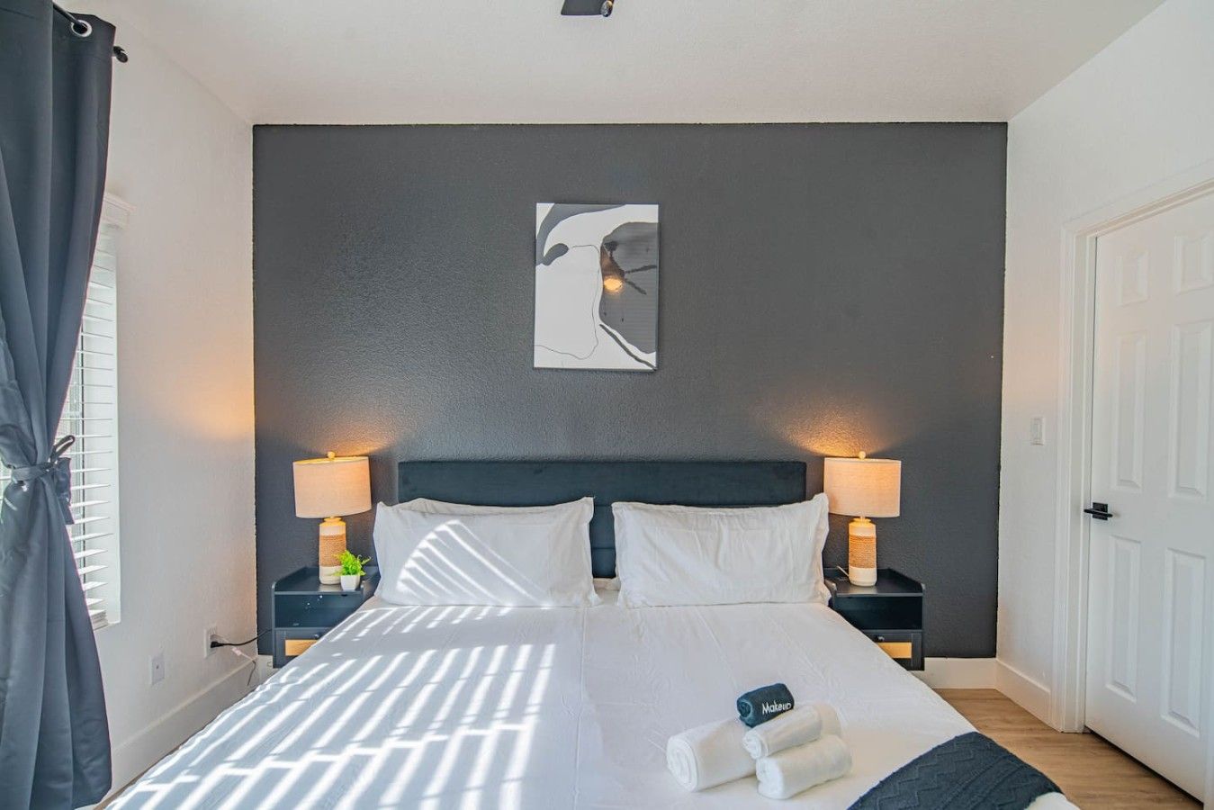 A hotel room with a bed, two bedside tables with lamps, a wall-mounted artwork, and a door.