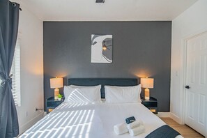 Une chambre d’hôtel comprenant un lit, deux tables de chevet avec des lampes, une œuvre d’art accrochée au mur et une porte.