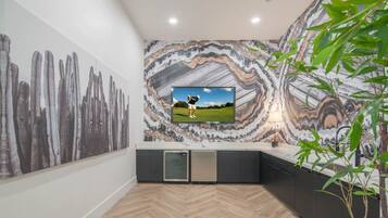 A modern kitchen with a large TV, a herringbone wood floor, and a marble backsplash.