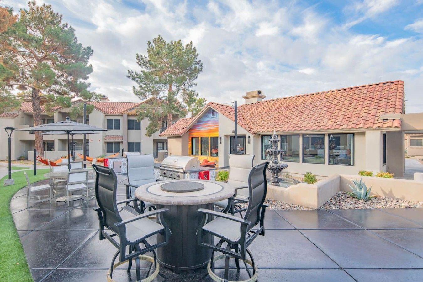 An outdoor patio with a round table and chairs, a grill, and a fountain.