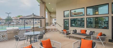 Une terrasse extérieure avec un barbecue, un coin salon et de grandes fenêtres.