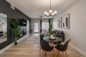 A modern living room with a dining area, a flat-screen TV, a chandelier, and a large window. - Modern Retreat Near TPC Pool, Spa, Pickleball W/D (Scottsdale)