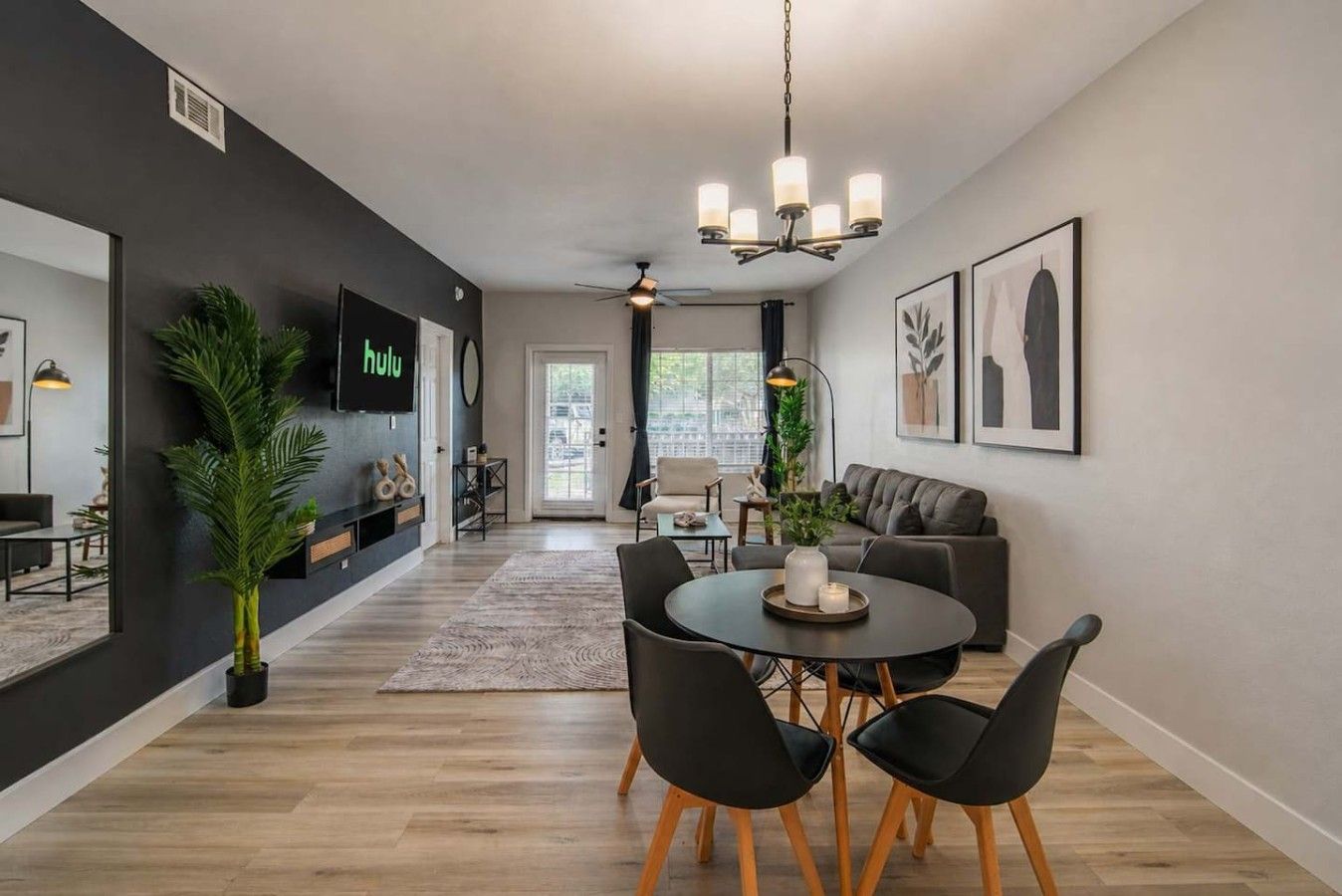 A modern living room with a dining area, a television mounted on the wall, and a ceiling fan.