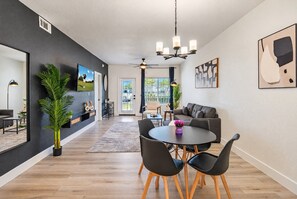 A modern living room with a dining area, a large TV, and a ceiling fan.