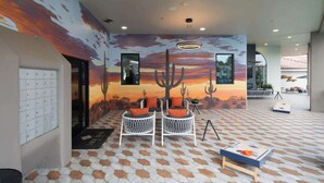 Un vestíbul amb un mural d'un capvespre al desert, dues cadires de vimet blanques amb coixinets taronja i un paviment estampat.