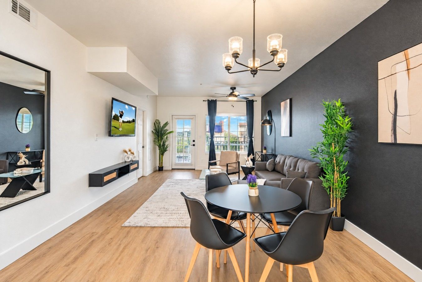 Un salon moderne comprenant un coin repas, un grand miroir, un téléviseur à écran plat et un ventilateur de plafond.