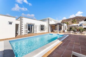 Una villa moderna con piscina, un porche cubierto y montañas al fondo.