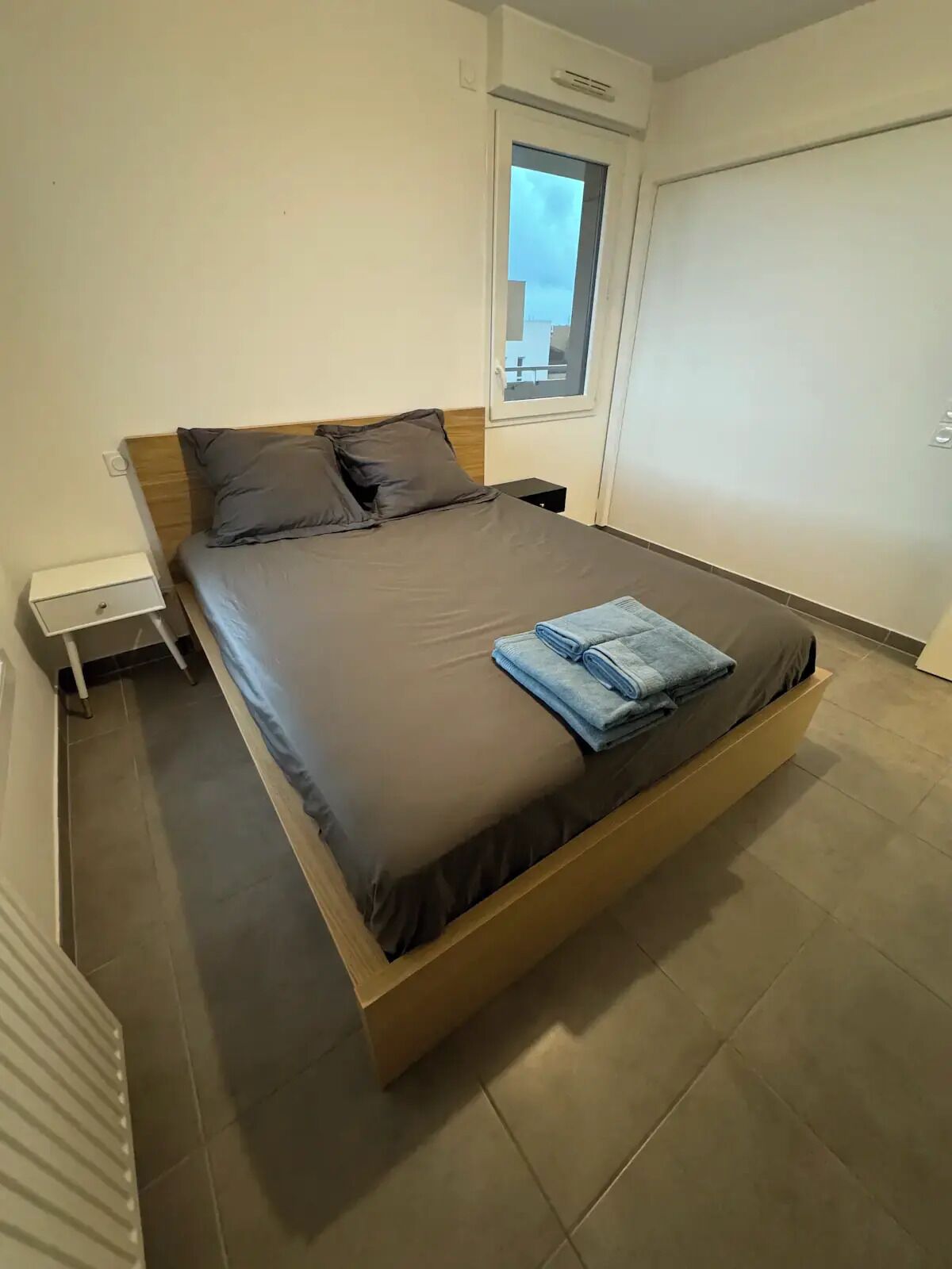 A modern bedroom with a large bed, a small bedside table, and a window.