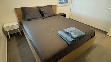 A modern bedroom with a large bed, a small bedside table, and a window.