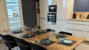 A modern dining area with a wooden table set for six, black chairs with gold accents, and a kitchen in the background with white cabinets and stainless steel appliances. - Luxurious 5 pc + Jacuzzi + rooftop + terrace + air conditioning (Montpellier)