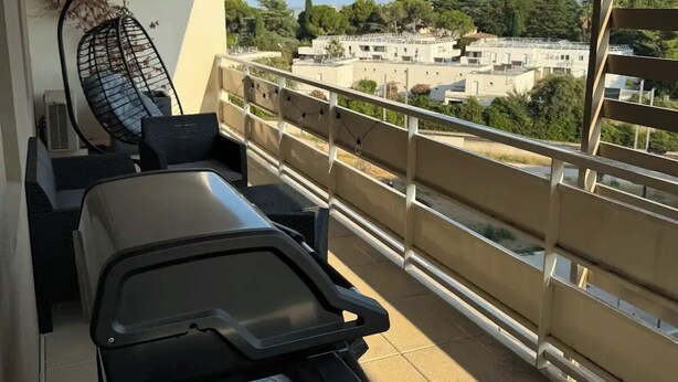 A balcony with a dining table, chairs, and a hanging chair. The balcony has a view of buildings and trees. - Luxurious 5 pc + Jacuzzi + rooftop + terrace + air conditioning (Montpellier)