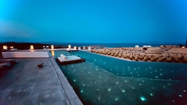 Una piscina con vista al mar, un área de descanso con sillones y un pequeño edificio al fondo.