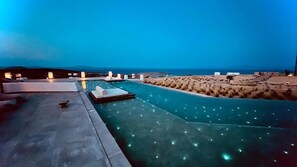 A swimming pool with a view of the sea, a lounge area with chairs, and a small building in the background. - Aeris suites pori (Naxos)
