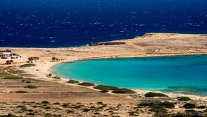 Un paisaje costero con un mar turquesa transparente, playa arenosa y vegetación escasa.