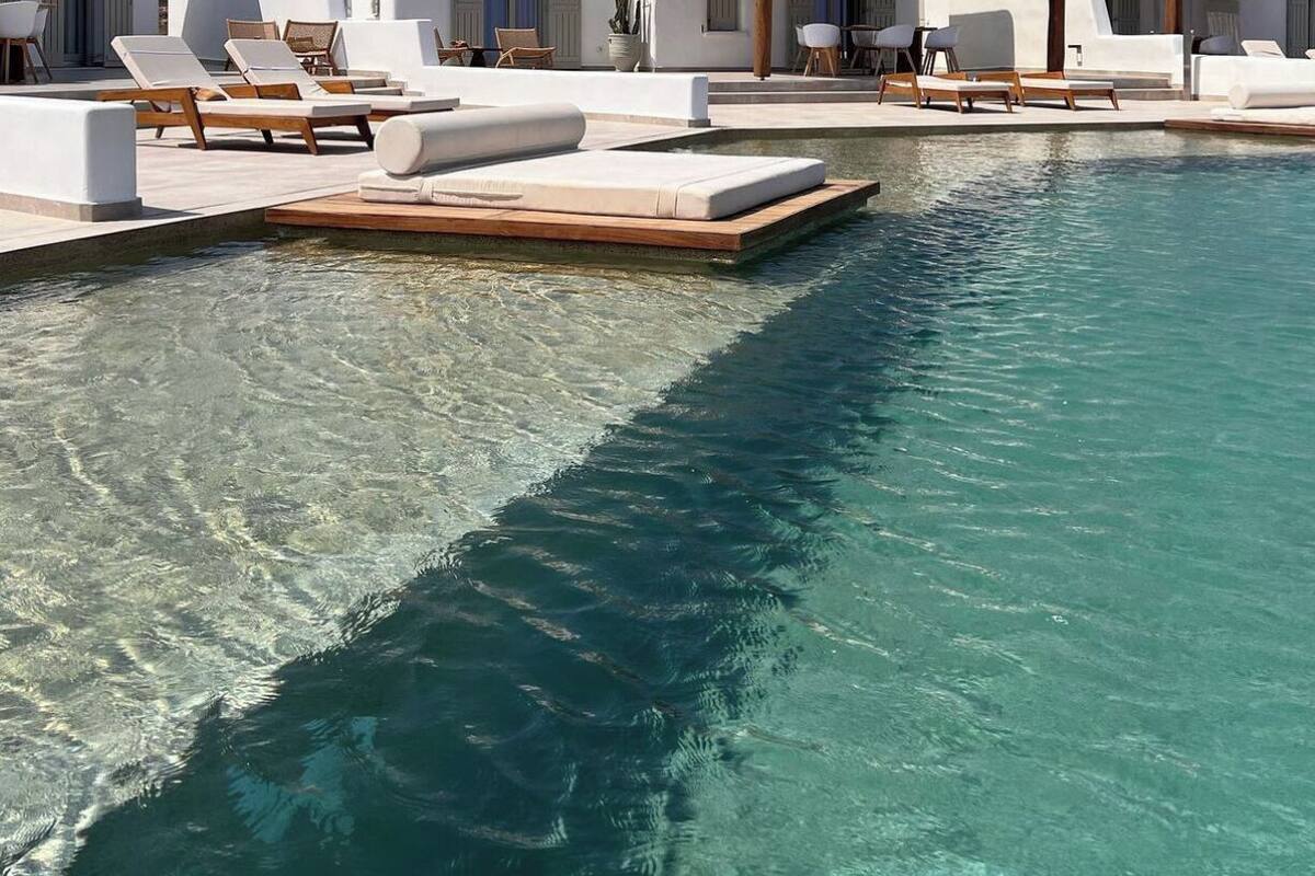 A modern resort with a clear pool, white buildings, and lounge areas with sunbeds.